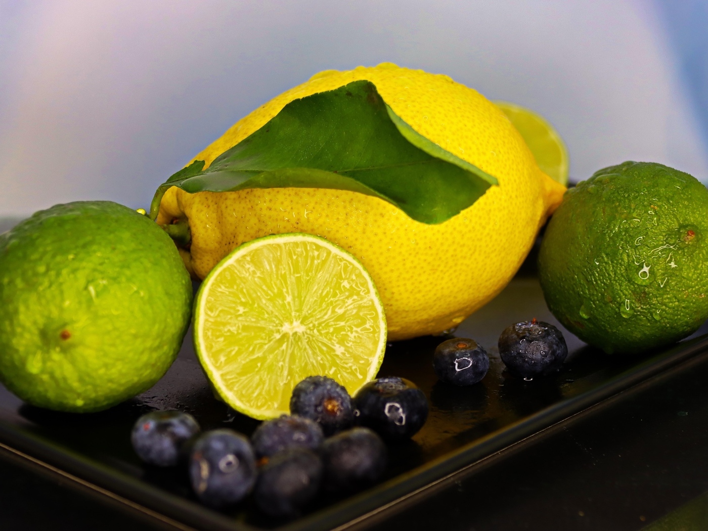 Желтый лимон на тарелке с лаймом и ягодами черники 