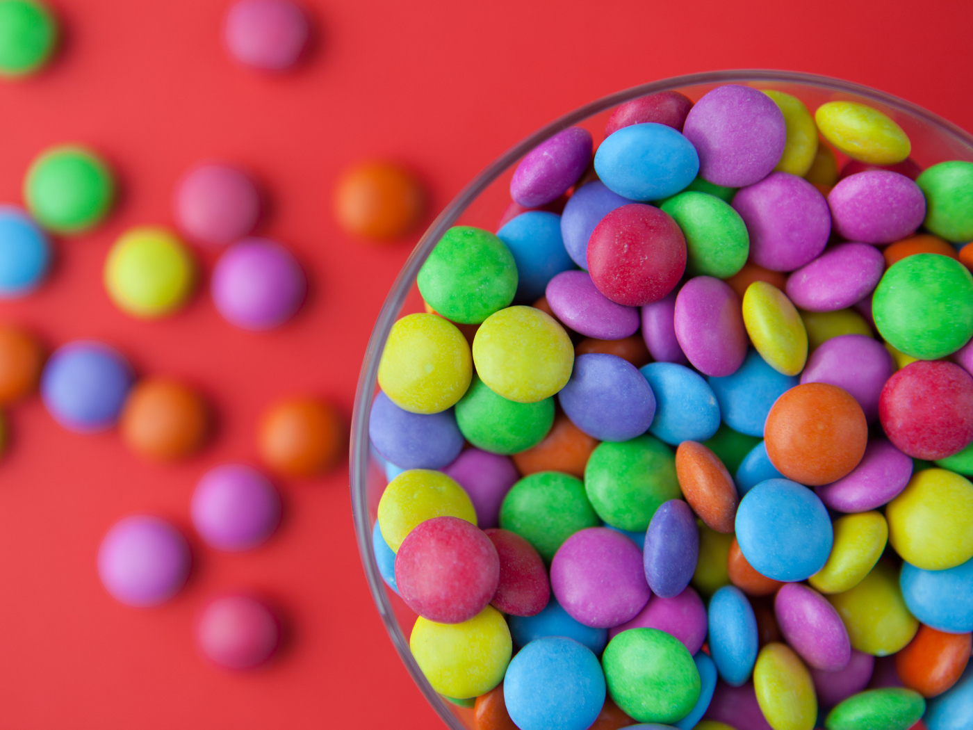 Разноцветные конфеты в стакане на красном столе