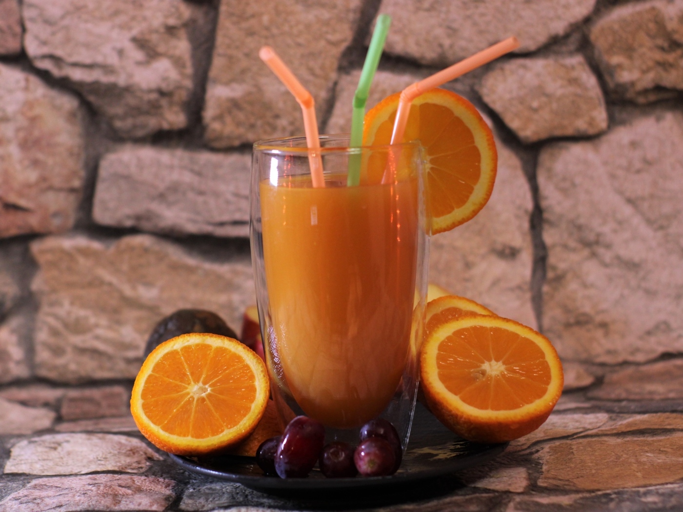 Стакан свежего сока с трубочками на столе с апельсинами