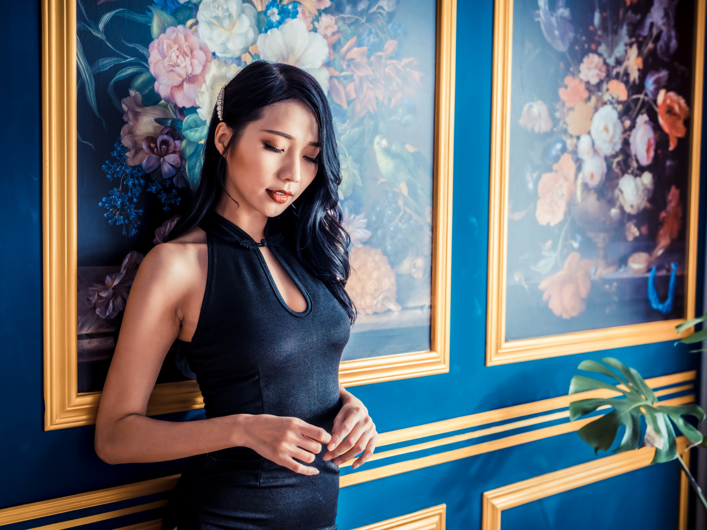 Красивая девушка азиатка в черном платье стоит у картины 