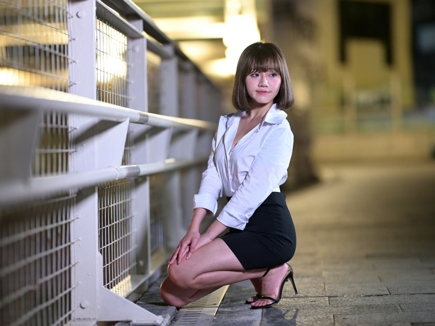 Азиатка в белой блузке и черной юбке сидит на корточках