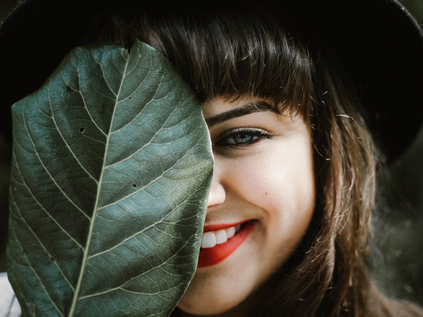 Милая улыбающаяся девушка прикрыла лицо листом