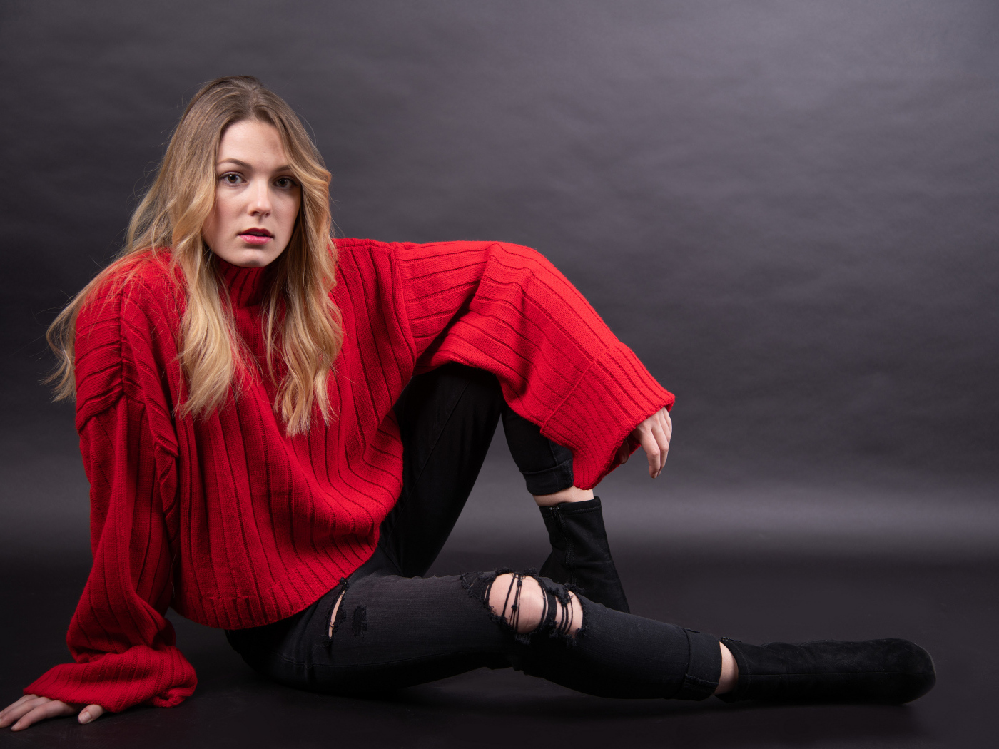 Девушка в красном свитере сидит на сером фоне