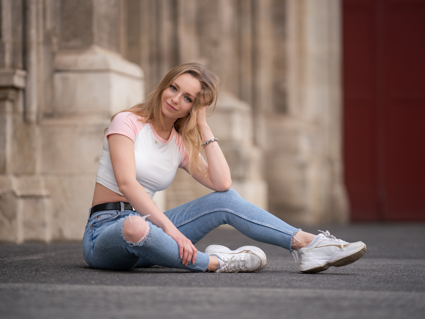 Девушка в рваных джинсах сидит на асфальте