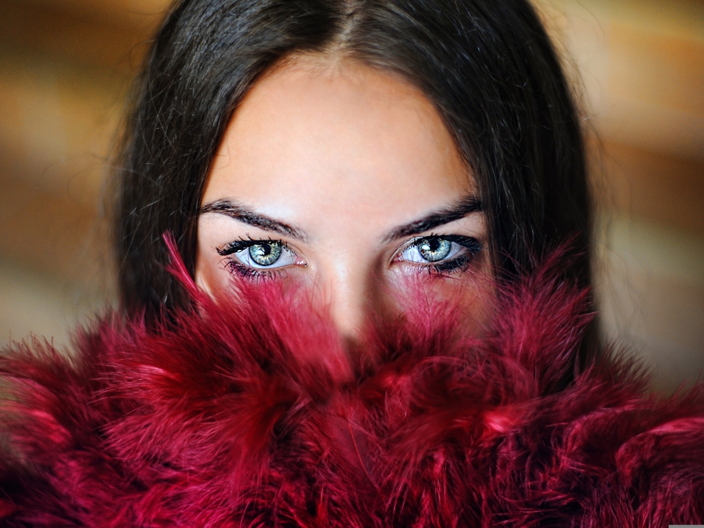 Девушка с красивыми глазами закрыла лицо красными перьями