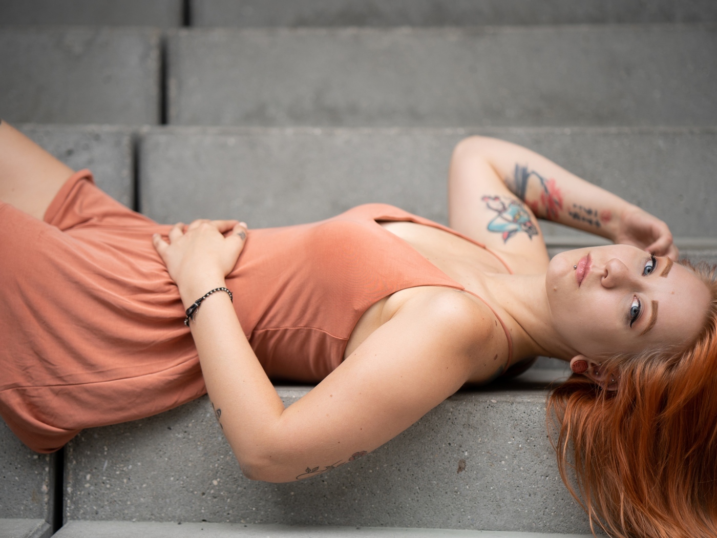 Рыжеволосая девушка с татуировками лижет на ступеньках