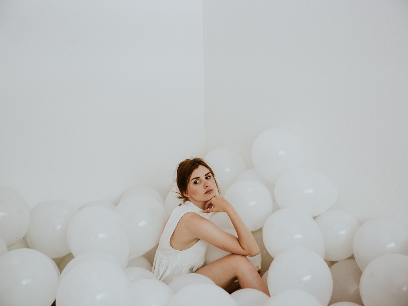 Грустная девушка сидит в белых воздушных шариках