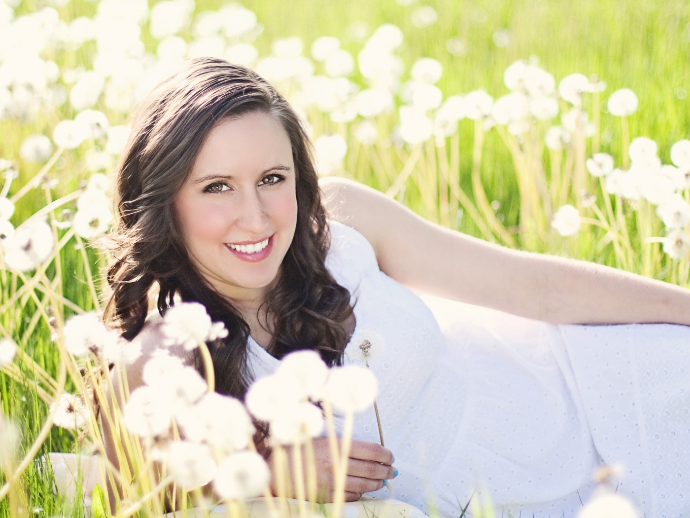 Улыбающаяся девушка лежит на поле с одуванчиками