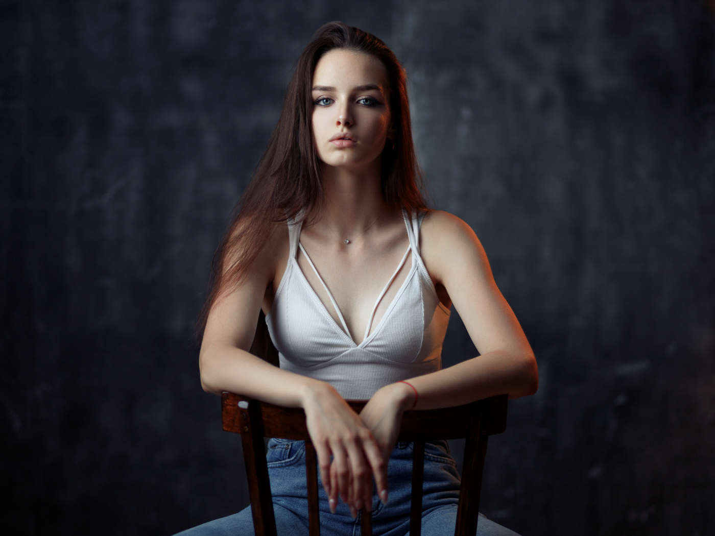 Молодая длинноволосая девушка сидит на деревянном стуле