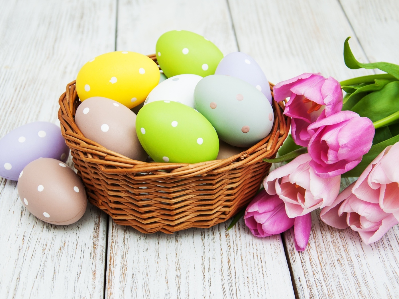 Корзина разноцветных яиц с тюльпанами на столе на Пасху