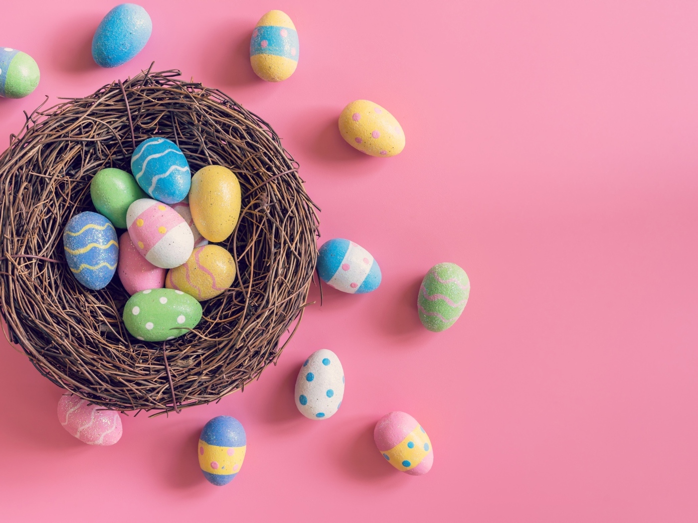 Гнездо с разноцветными яйцами на розовом фоне на Пасху
