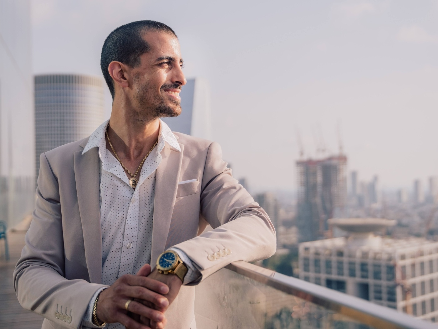 Улыбающийся стильный мужчина в костюме стоит на балконе 