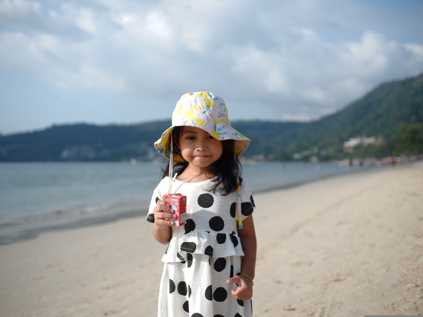 Девочка с соком в руках стоит на пляже