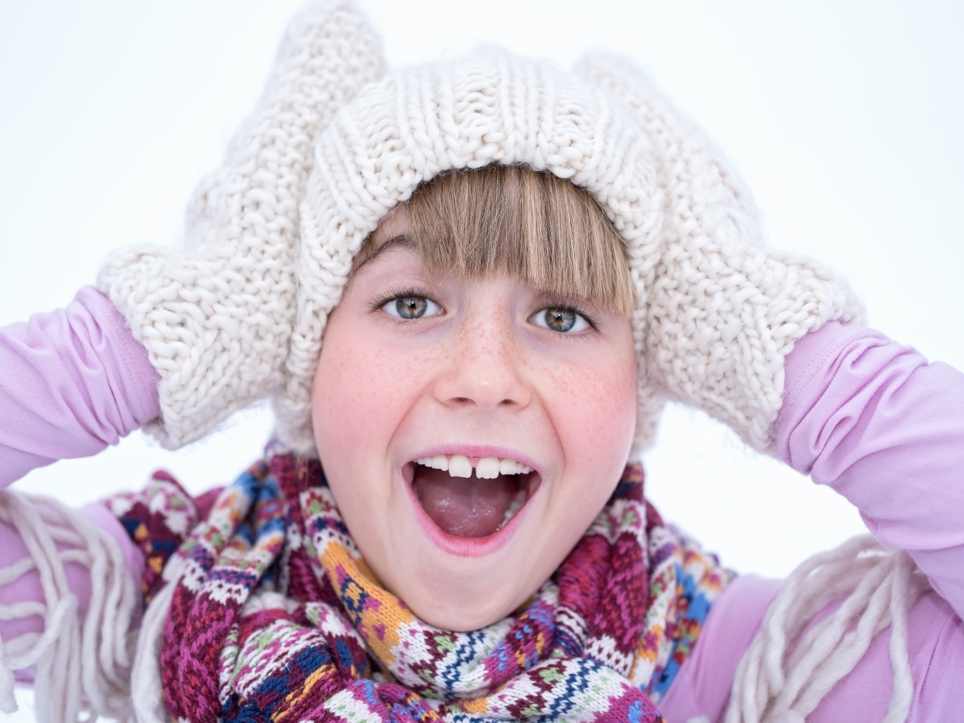 Довольная девочка в вязаной шапке и варежках