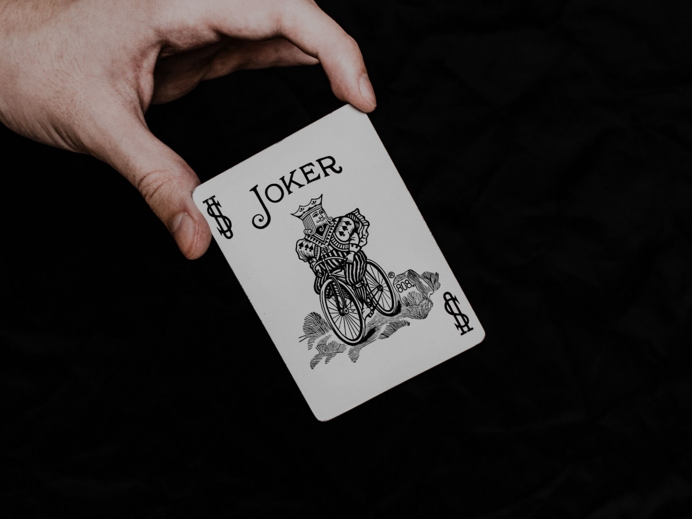 Карта Джокер в руке на черном фоне