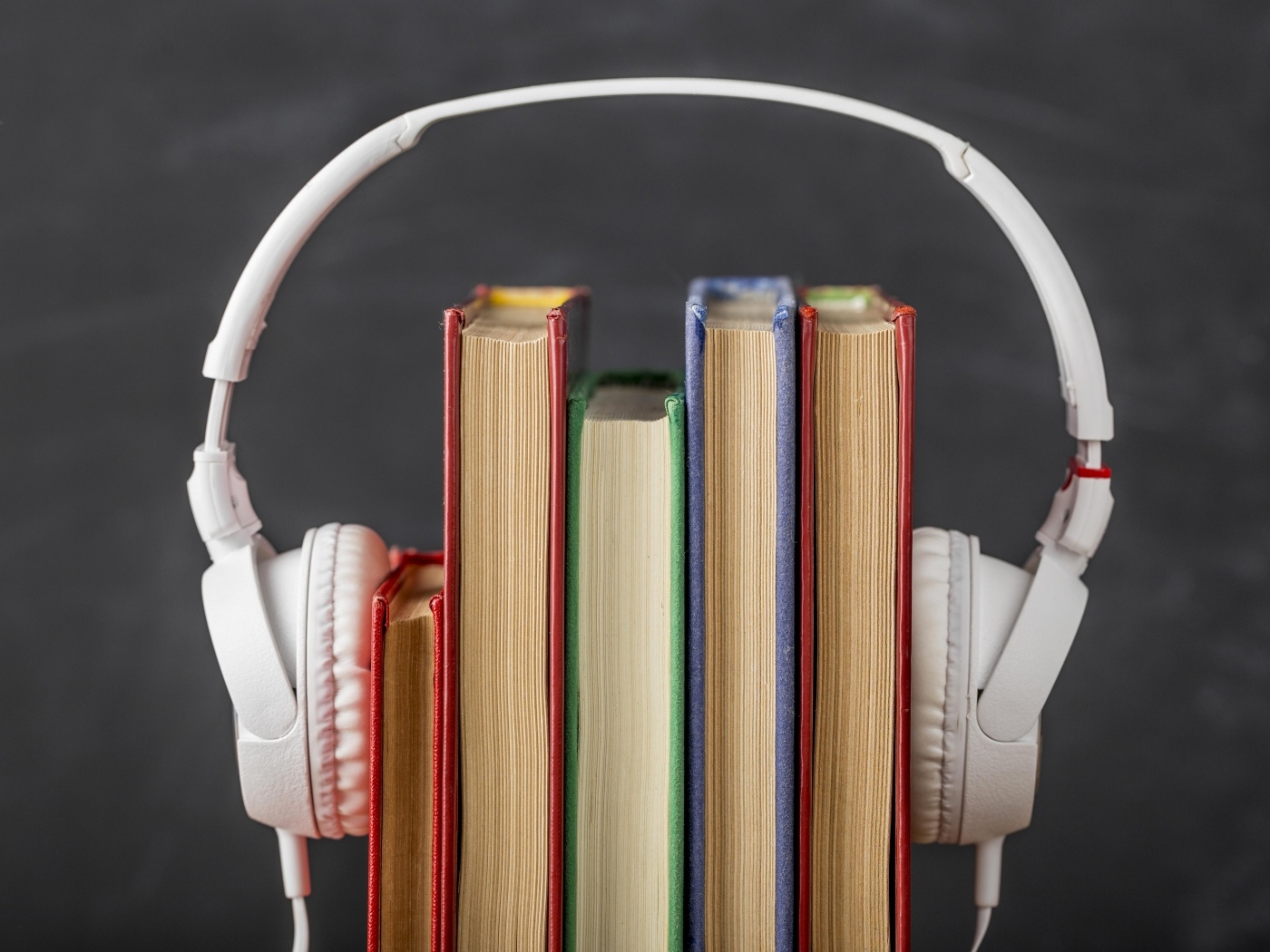 Разноцветные книги с белыми наушниками на сером фоне