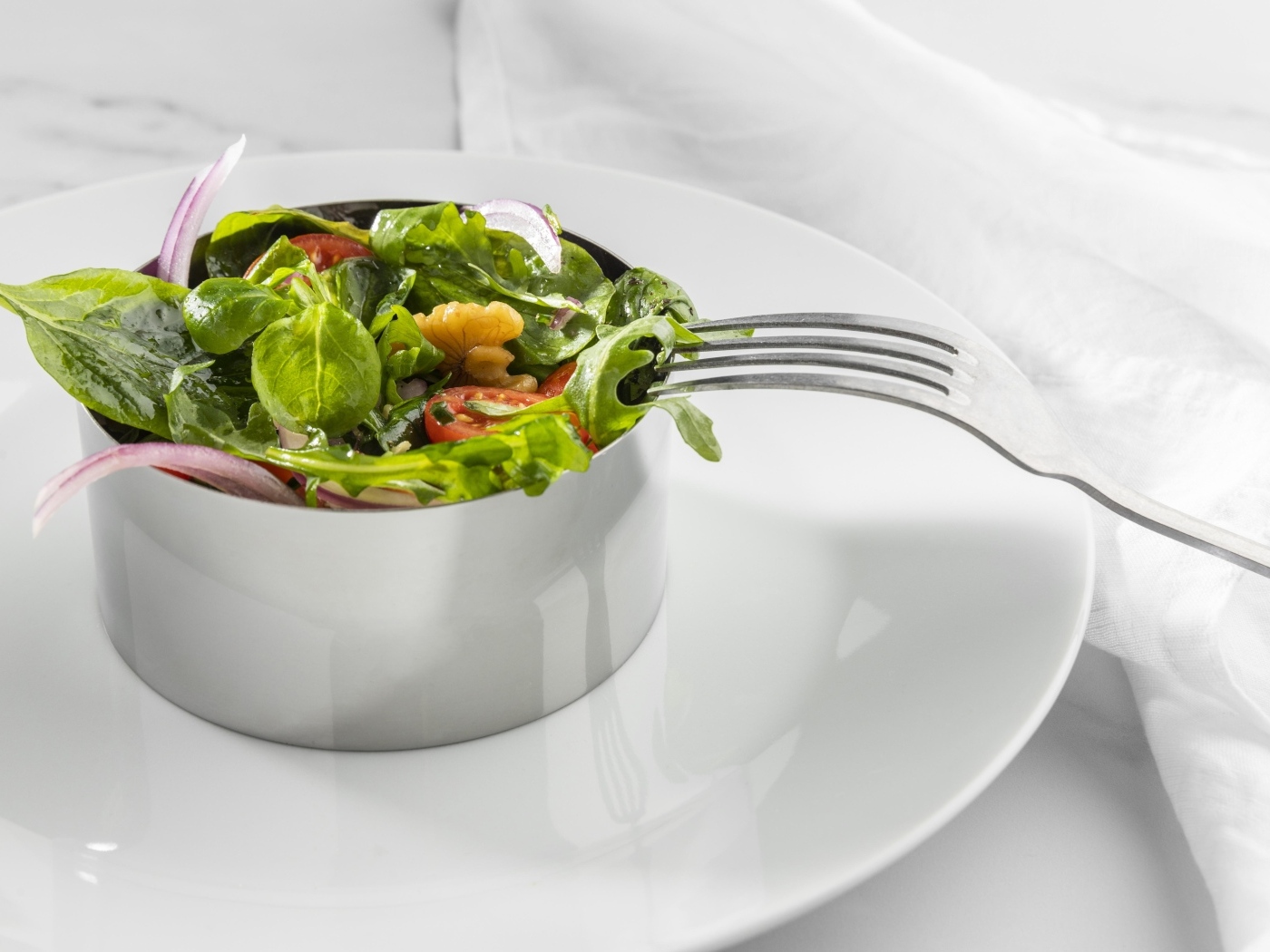 Зеленый салат с орехами на большой белой тарелке