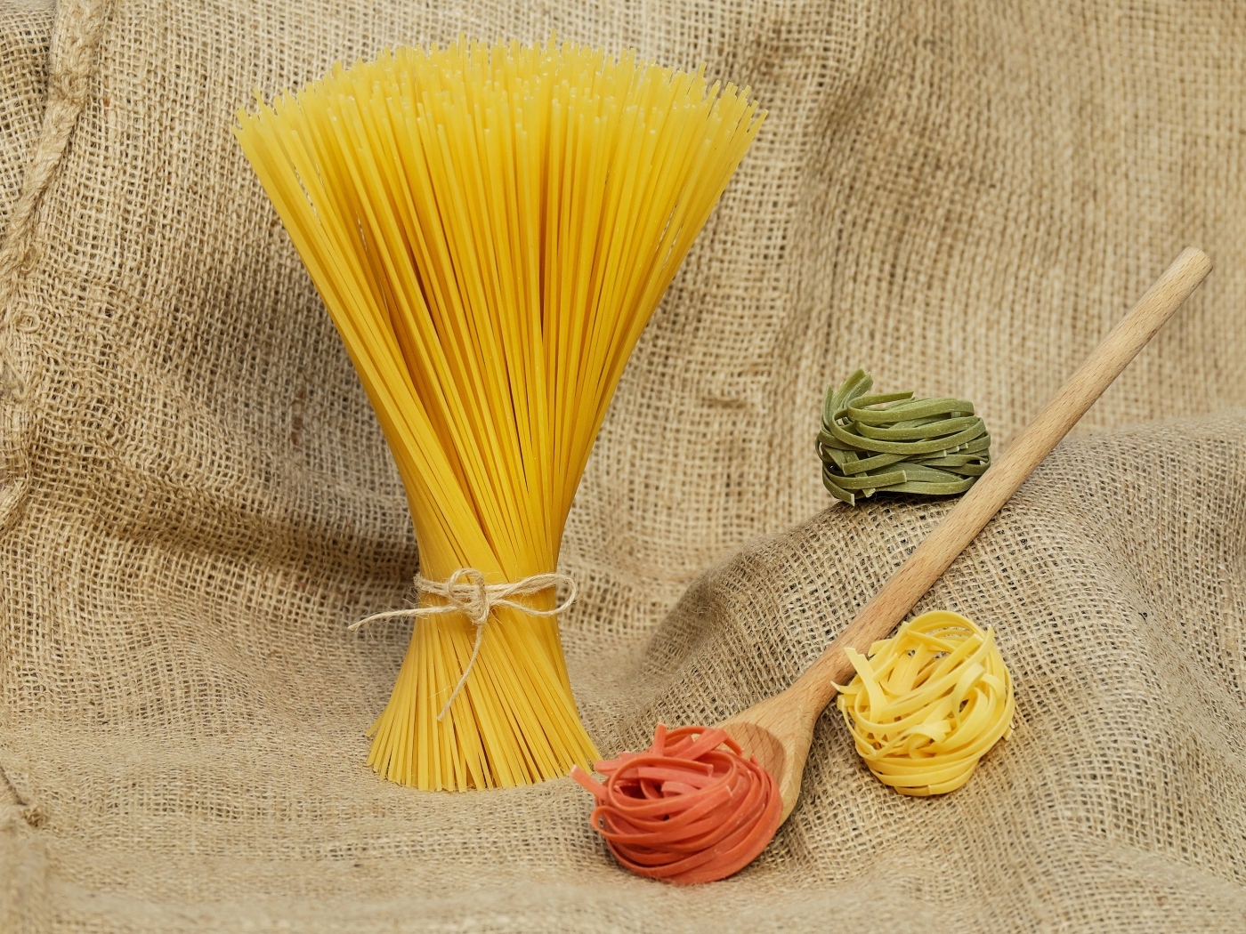 Разноцветные макаронные изделия с деревянной ложкой на мешке