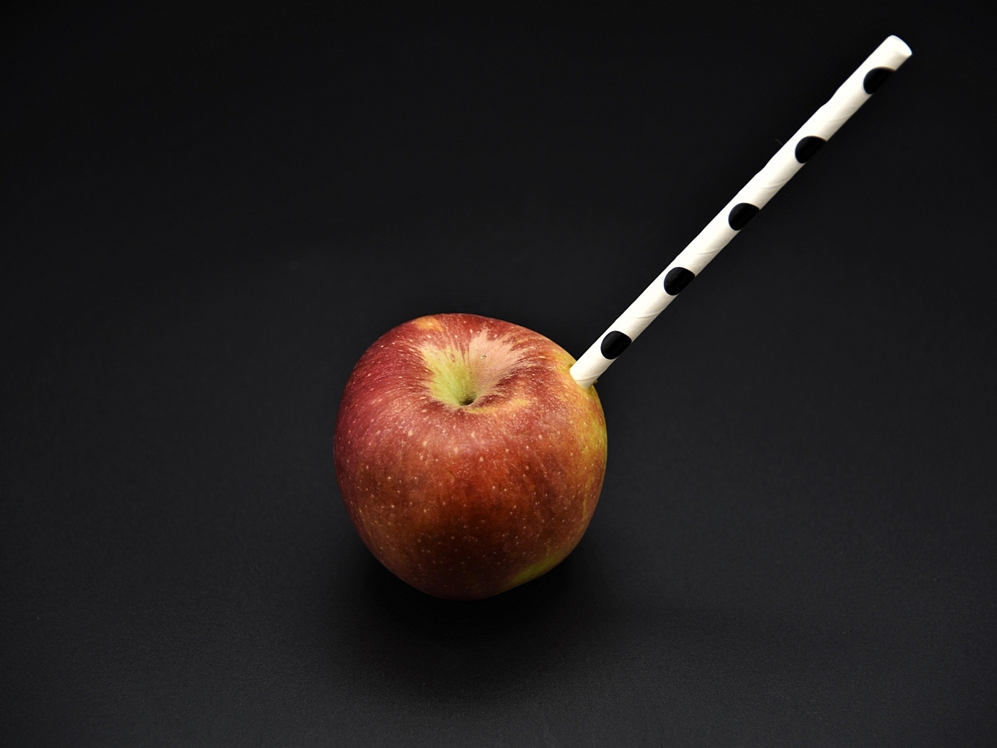 Большое красное яблоко с трубочкой на черном фоне