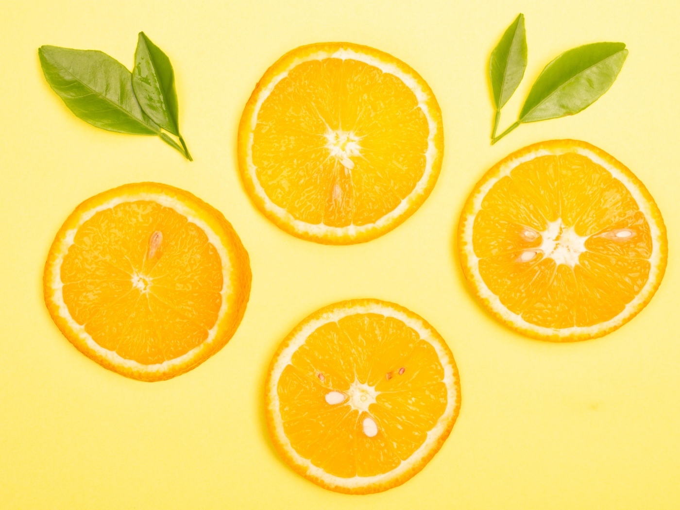 Нарезанный апельсин с зелеными листьями на желтом фоне