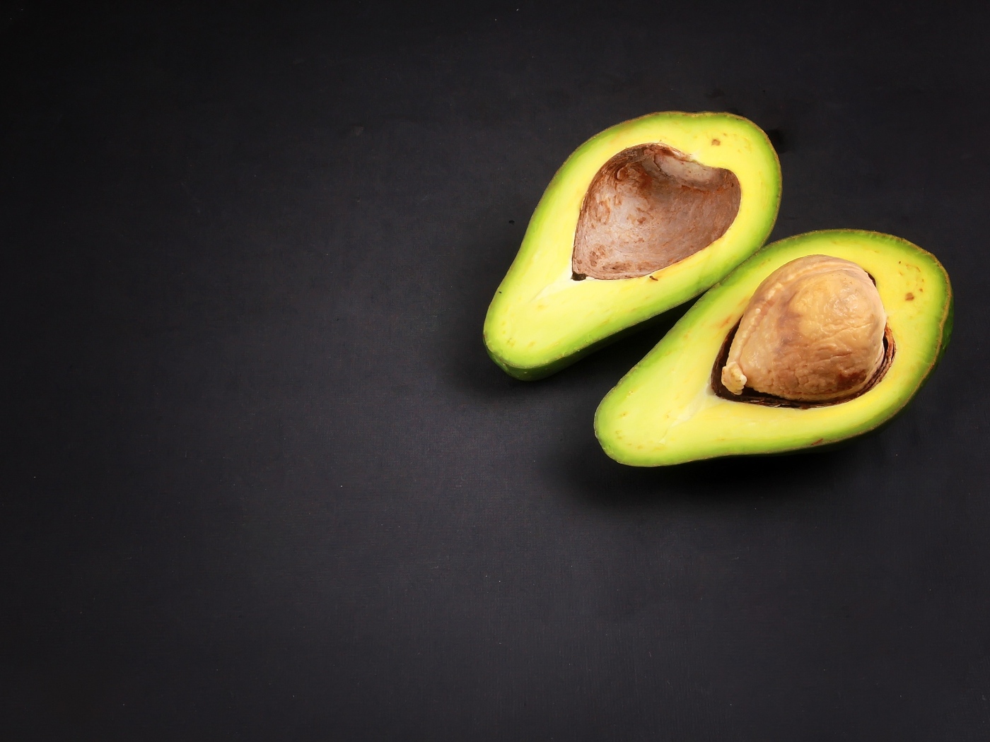 Две половинки зеленого авокадо на сером столе