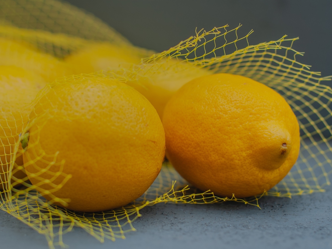 Желтые лимоны в сетке на сером столе