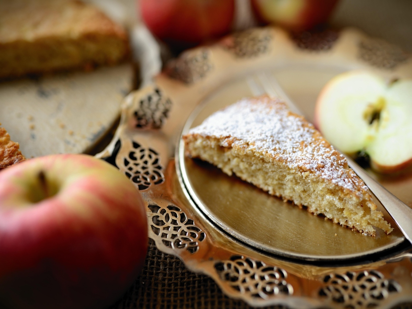 Кусок пирога с сахарной пудрой на столе с яблоками