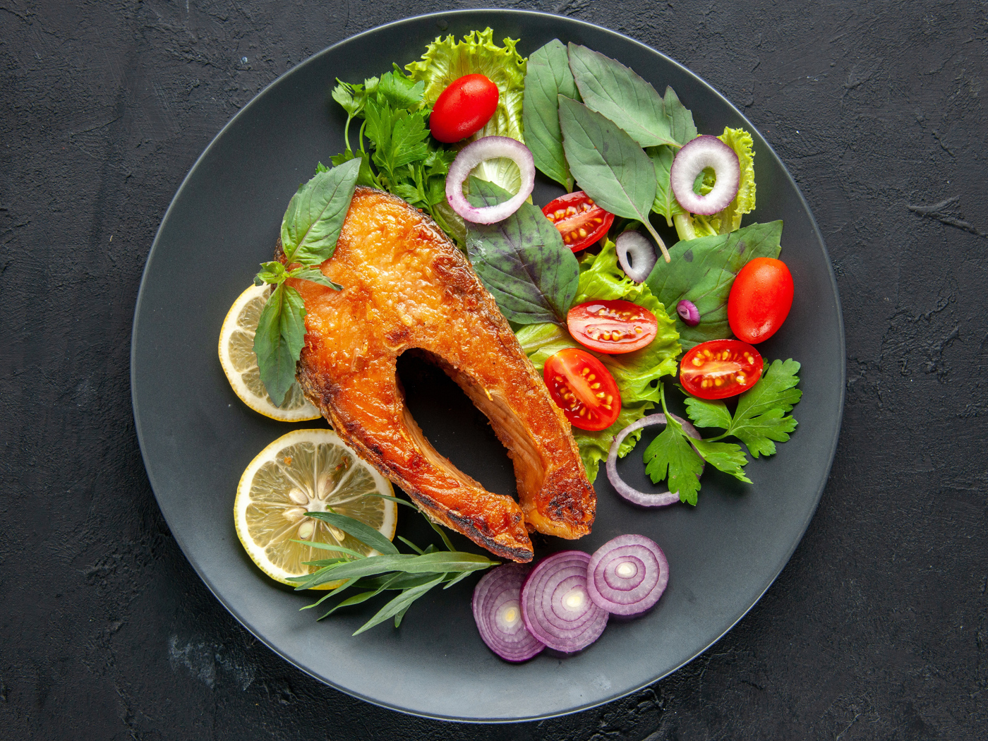 Жареная рыба на тарелке с зеленью,  лимоном и помидорами