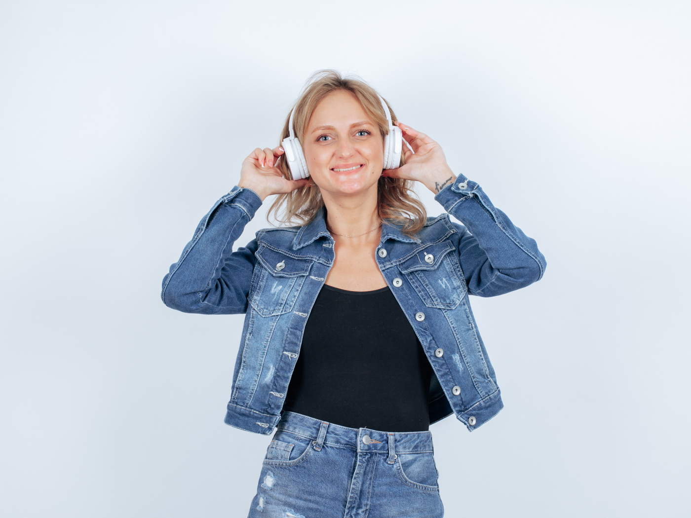Девушка в джинсовом костюме с наушниками на голове на фоне стены