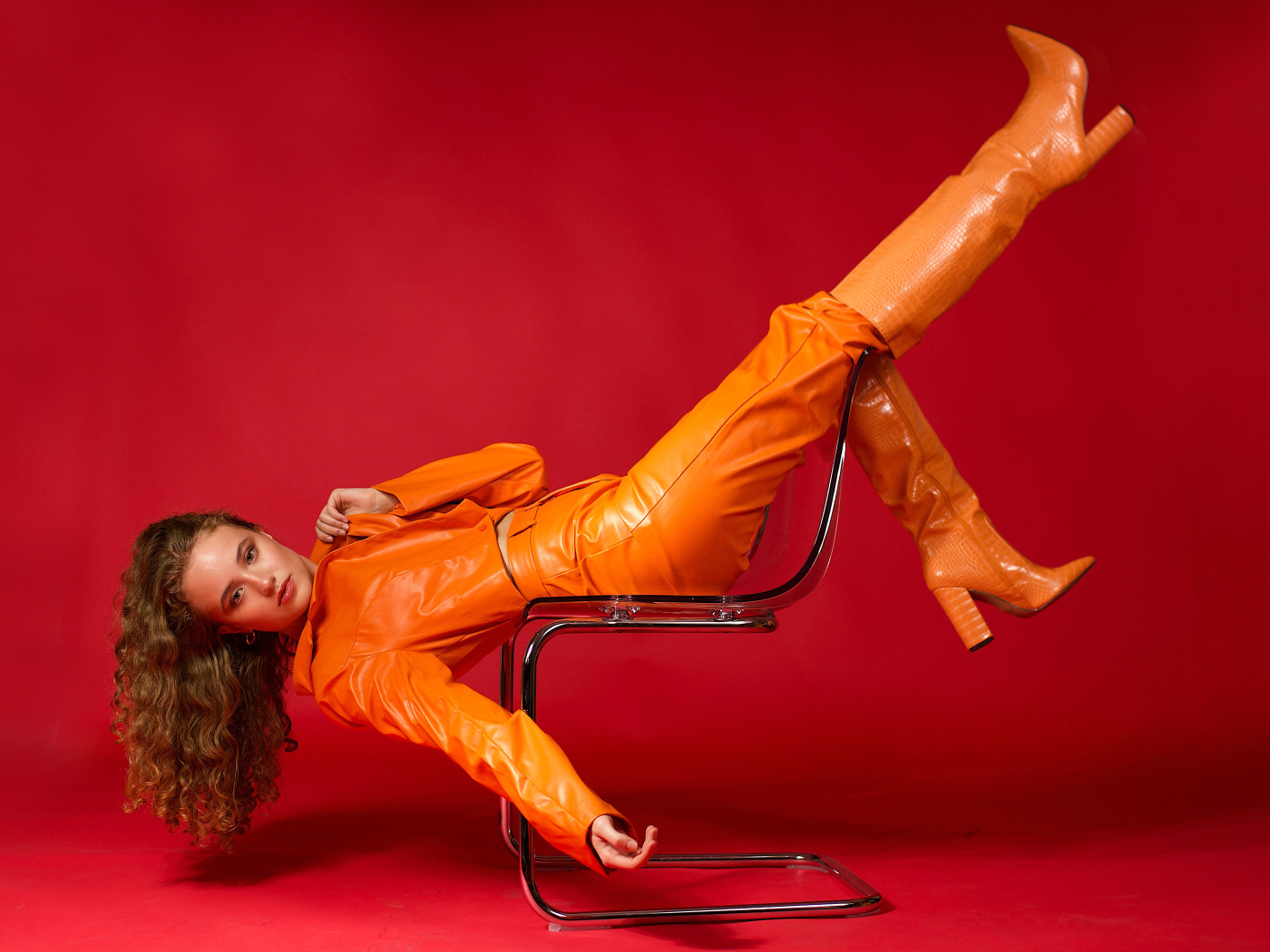Девушка в кожаном костюме лежит на кресле на красном фоне