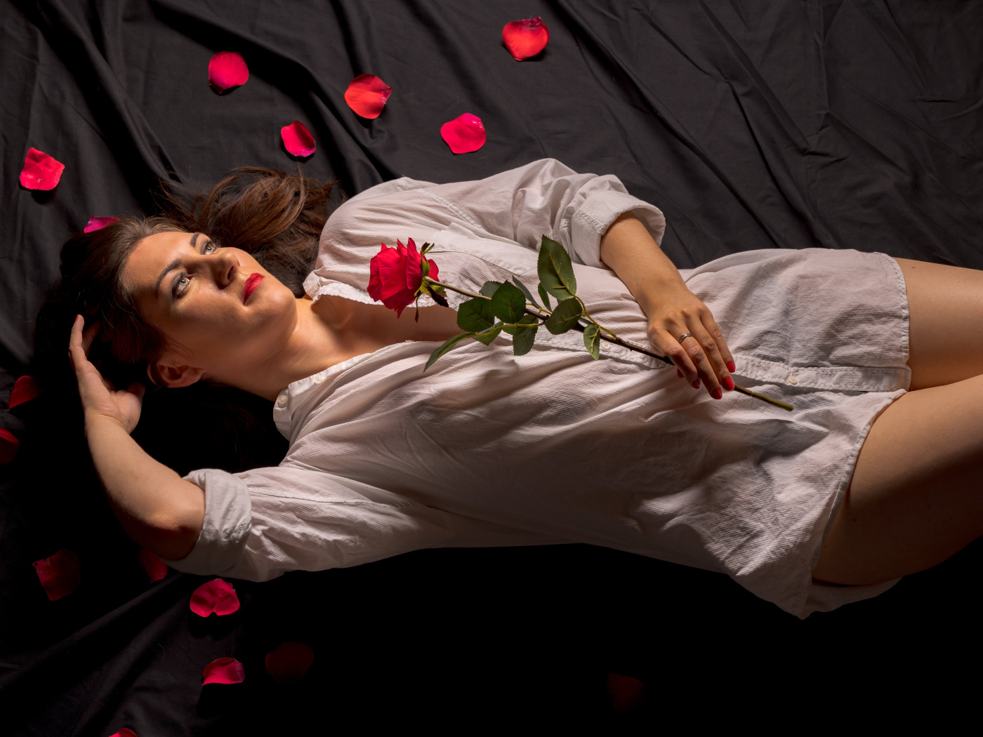 Девушка в белой рубашке с розой в руках лежит на постели