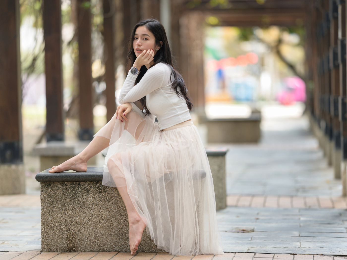 Девушка азиатка в белой юбке из фатина сидит на лавке