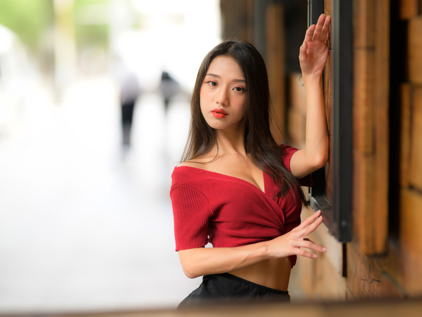 Азиатка в красном топе стоит у стены