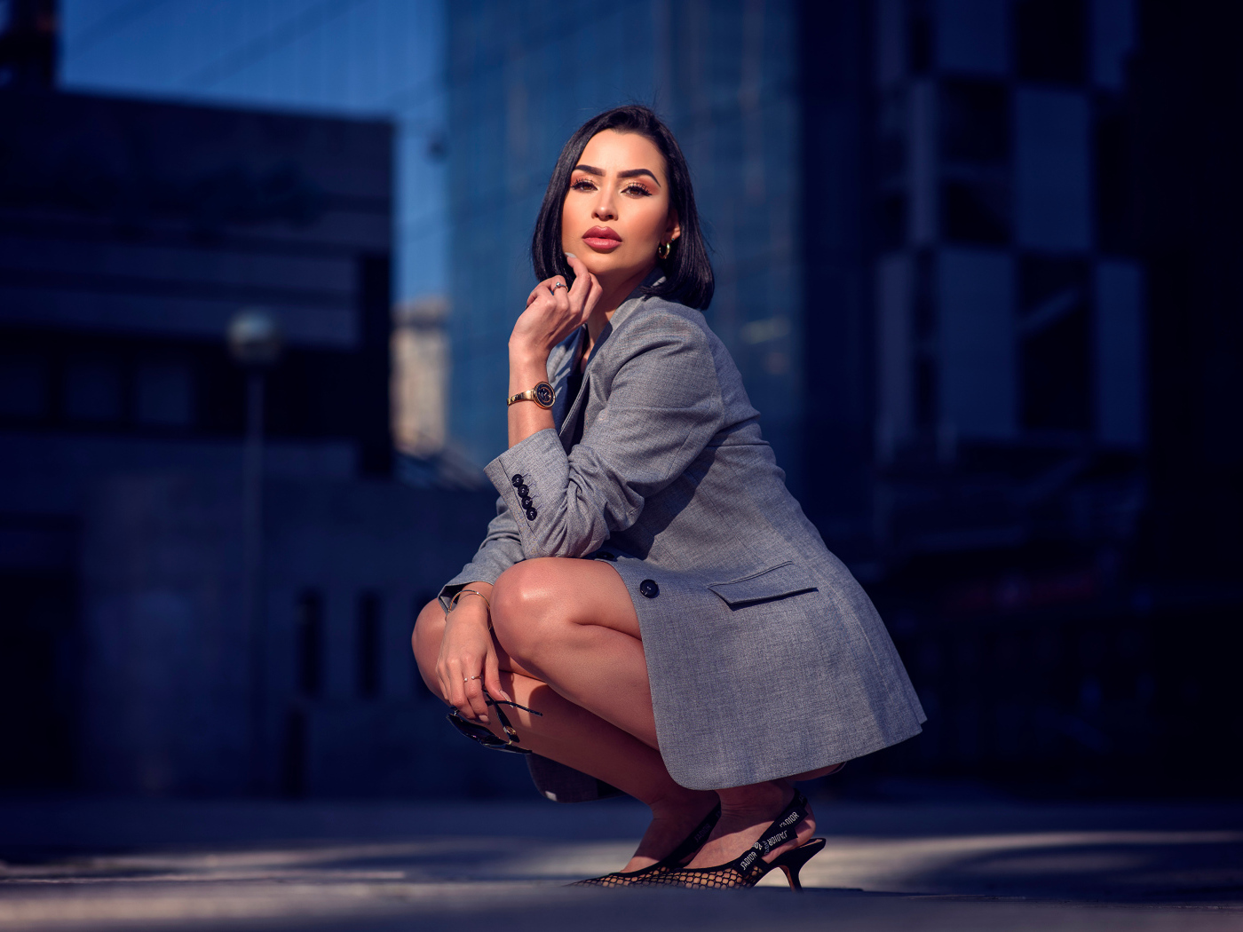 Красивая брюнетка в сером пиджаке сидит на корточках