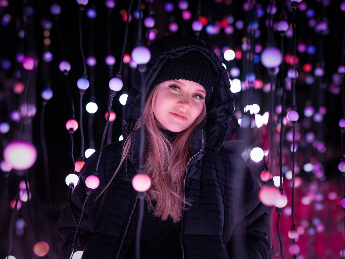 Девушка в черной куртке у светящейся гирлянды