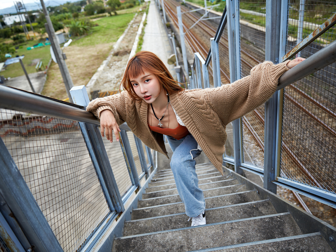 Рыжеволосая азиатка в кофте стоит на ступеньках