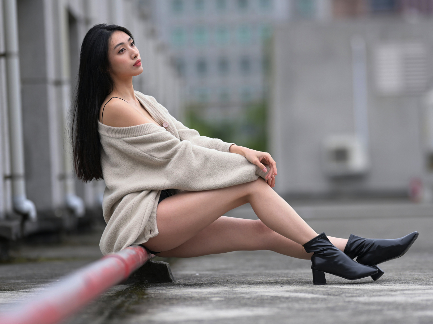 Грустная азиатка в теплой кофте сидит на трубе