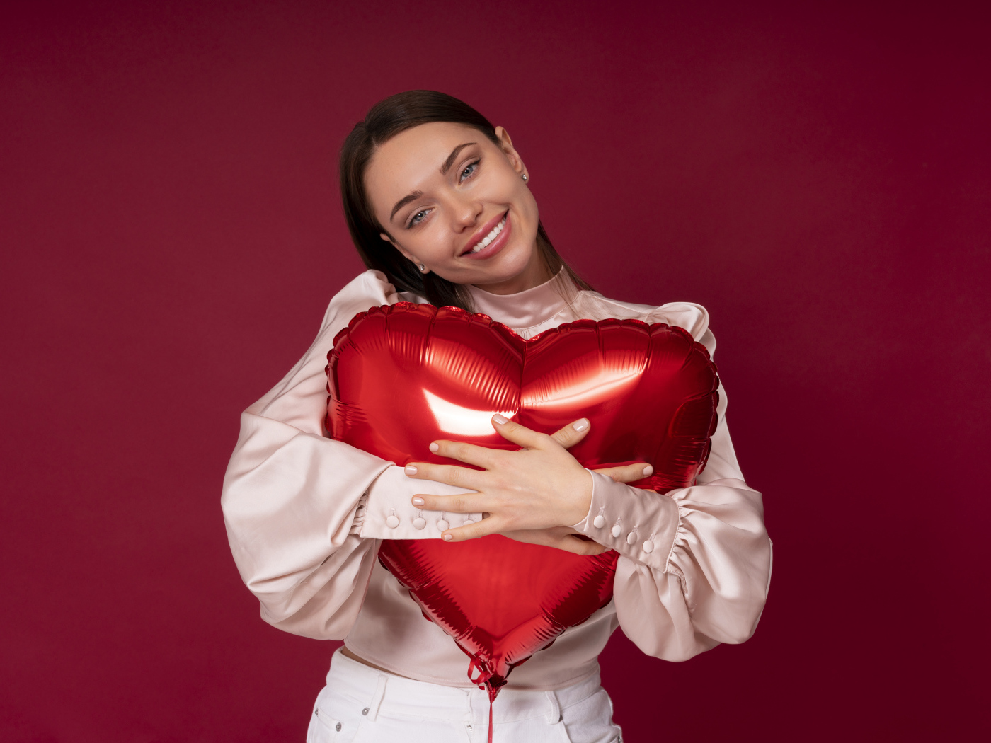 Улыбающаяся девушка обнимает шар в форме сердца