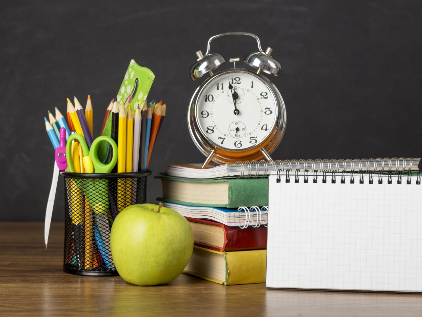 Канцелярские предметы на столе с будильником и книгами 