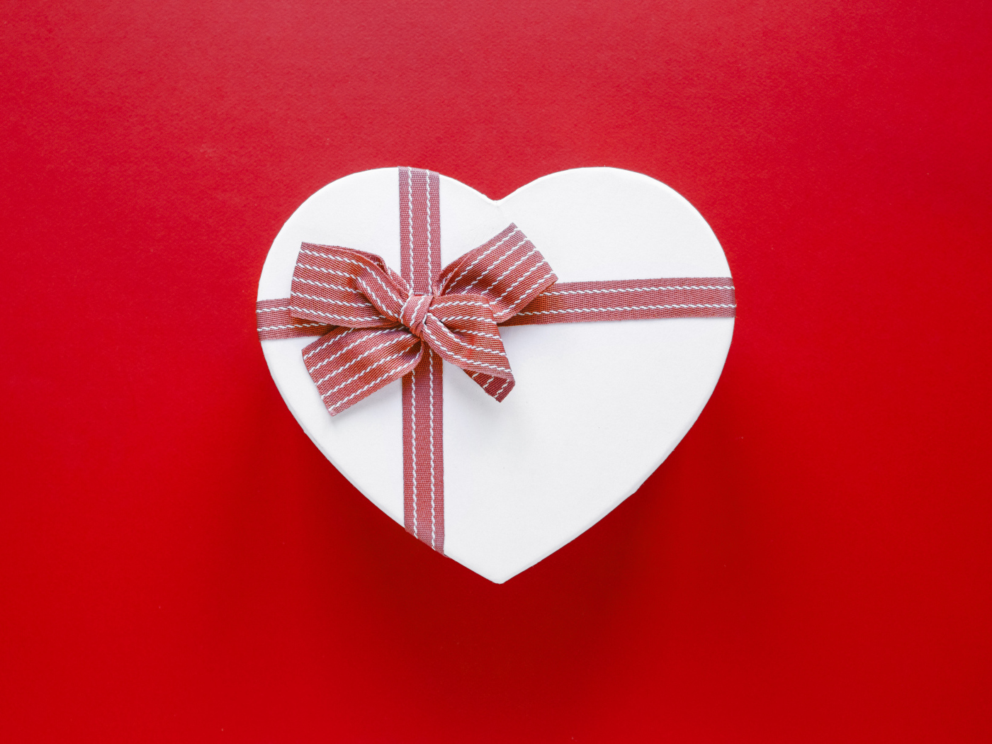 Белая коробка в форме сердца с бантом на красном фоне