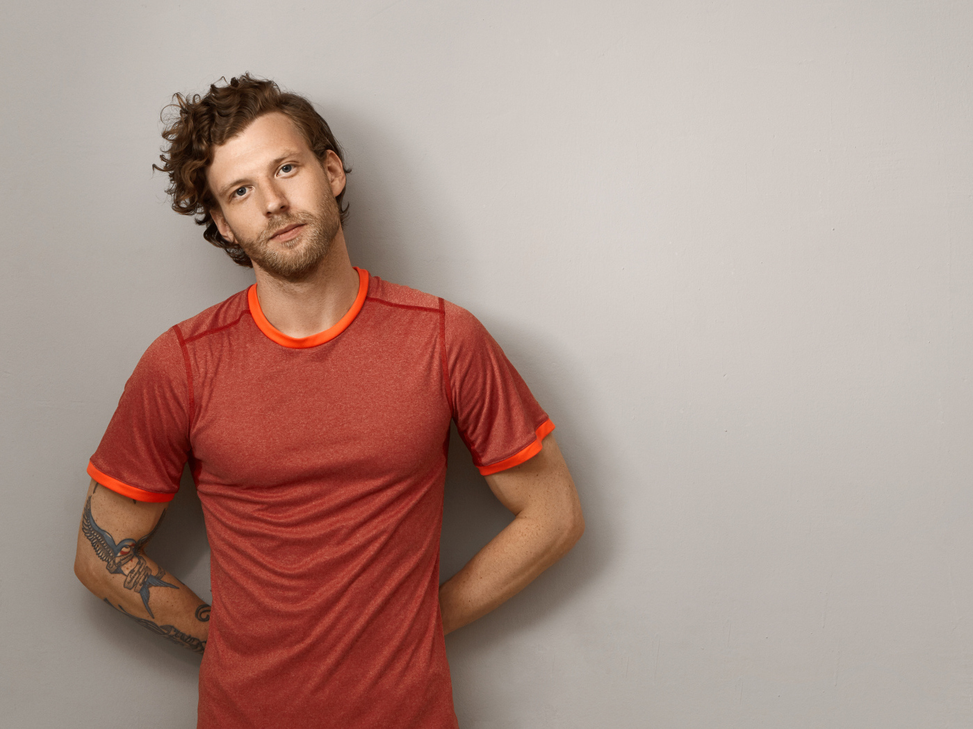 Мужчина в футболке стоит у серой стены