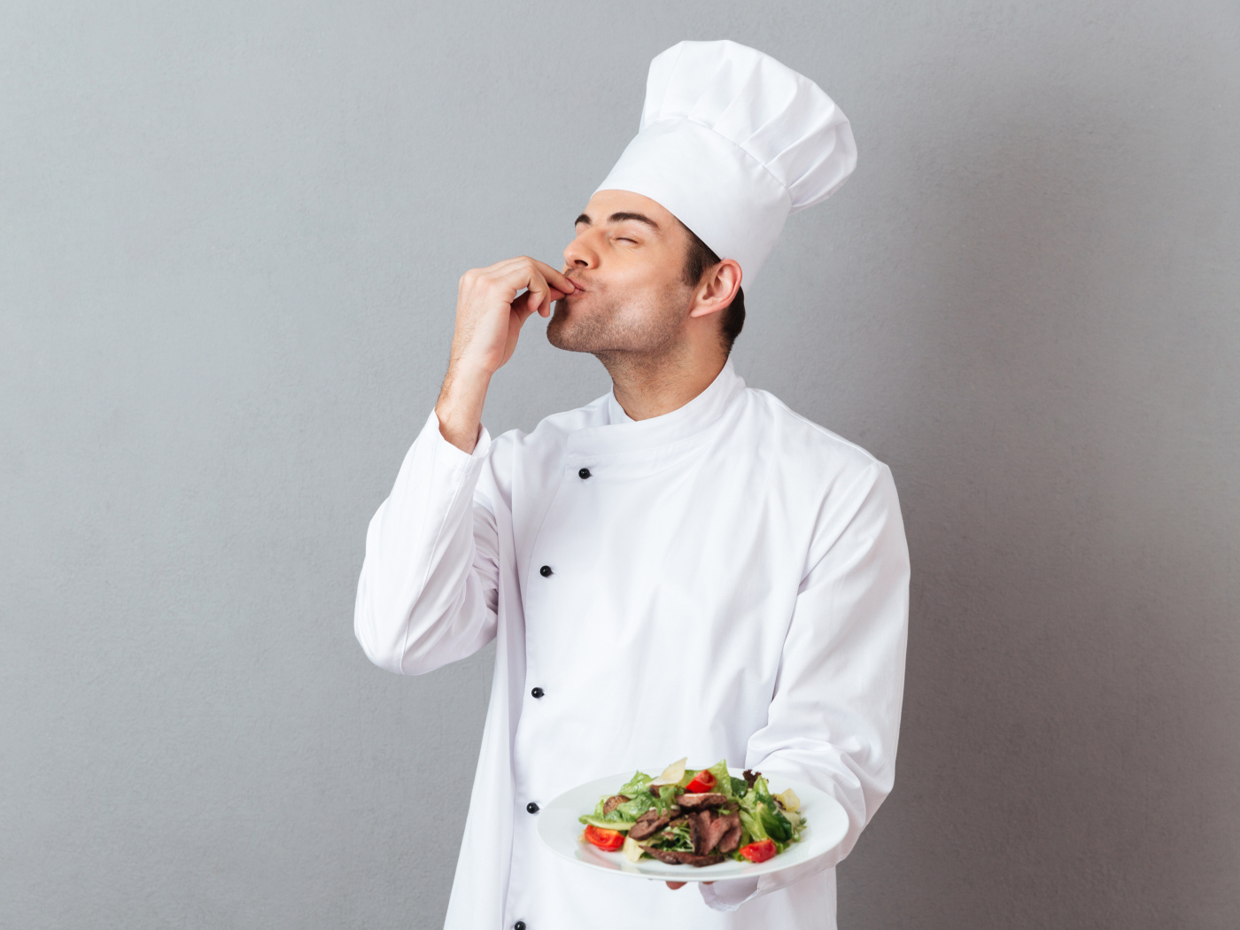 Мужчина повар в белом костюме с блюдом на сером фоне