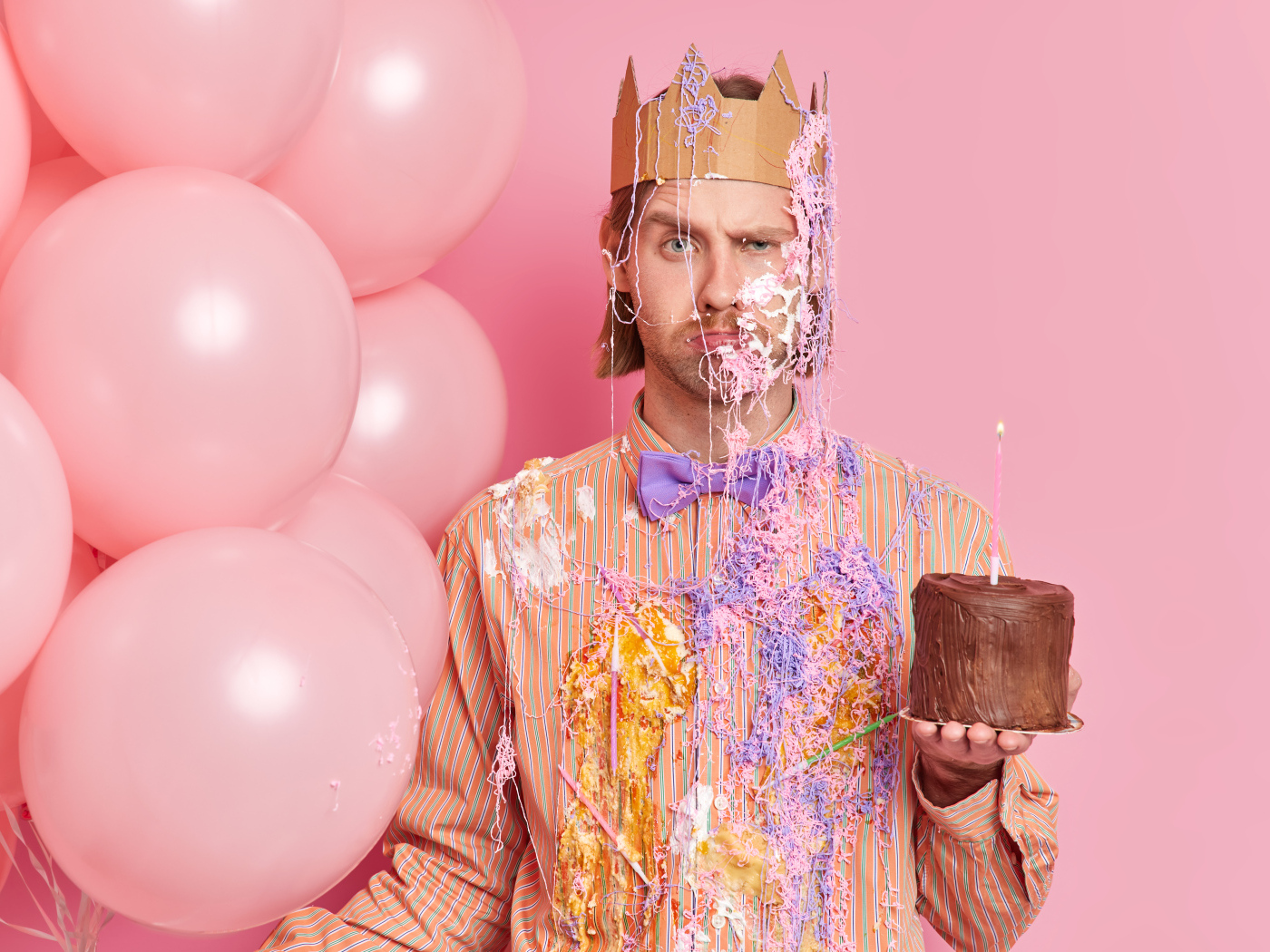 Мужчина принц с тортом и шариками на розовом фоне