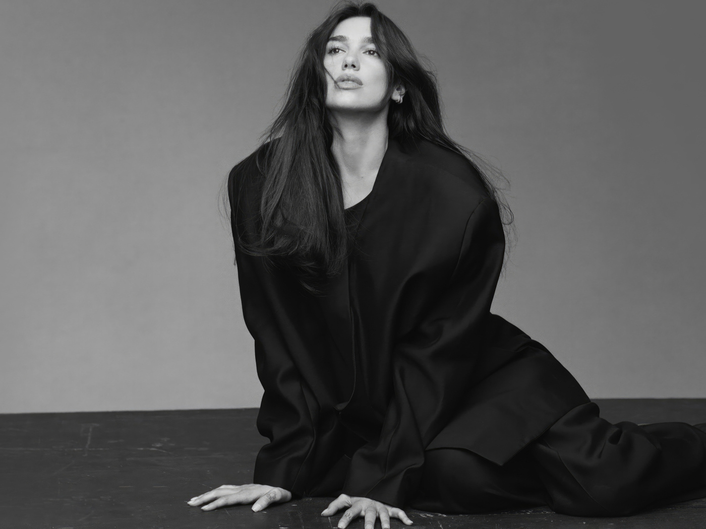 Певица Дуа Липа в черном костюме сидит на полу