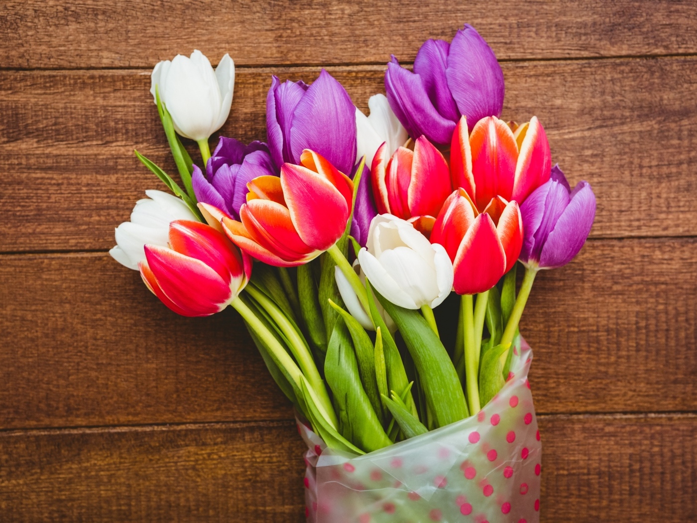 Букет разноцветных тюльпанов в пакете на деревянном фоне