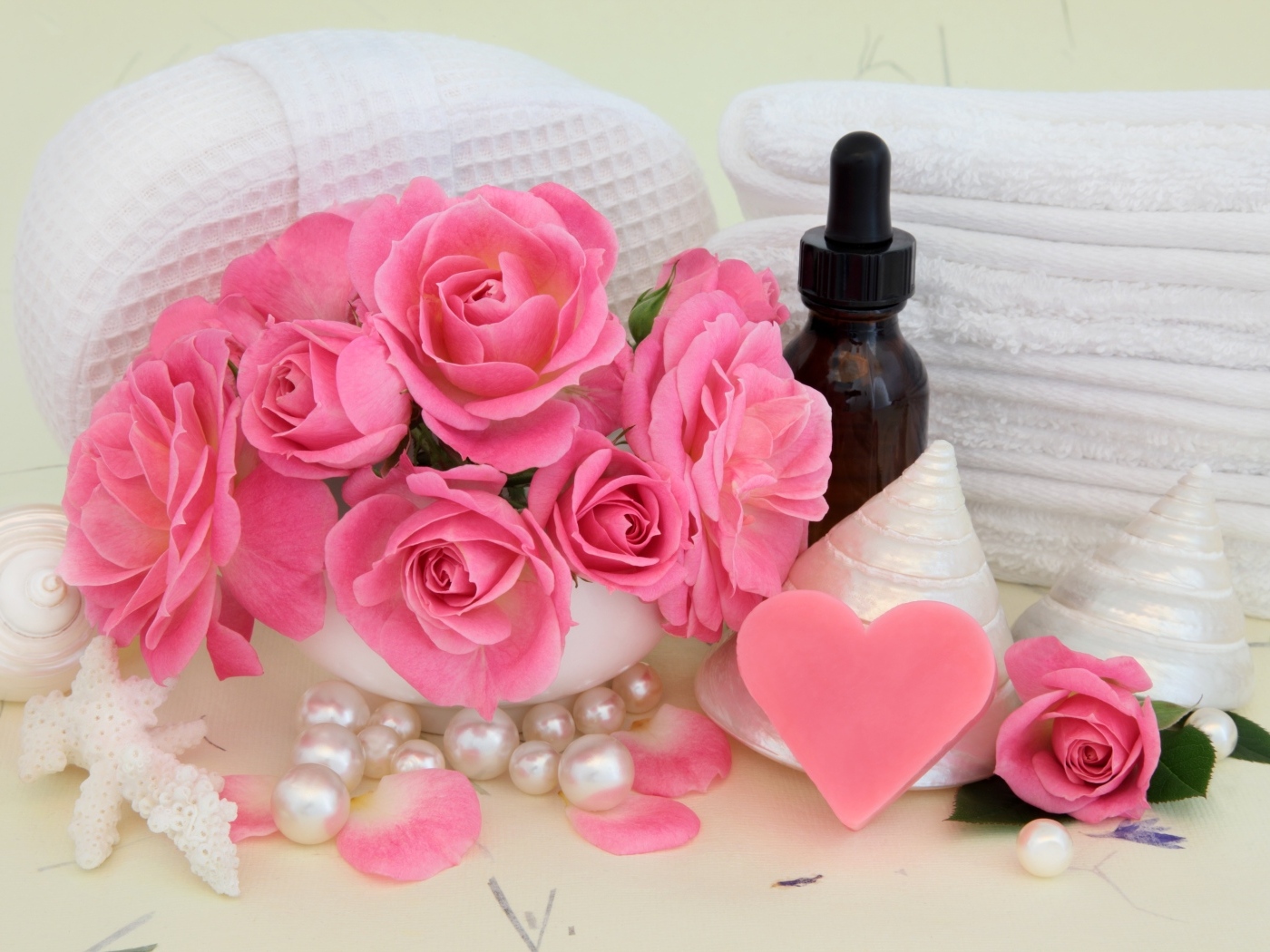 Розовые розы с полотенцами, ракушками и маслом на столе