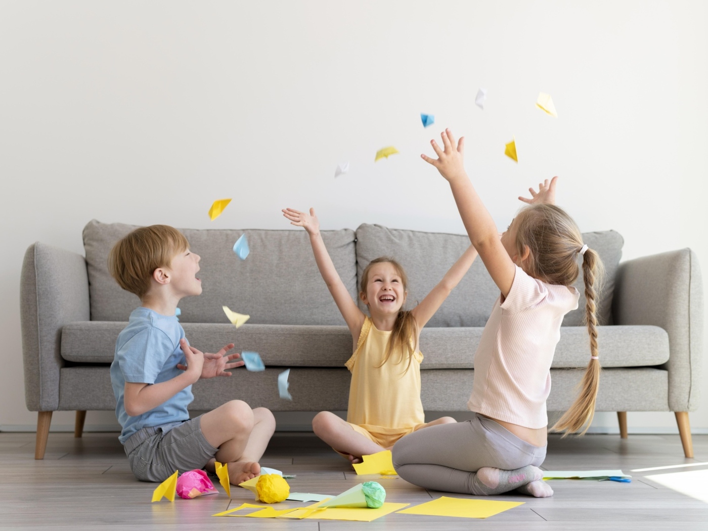 Дети играют на полу  в комнате с серым диваном