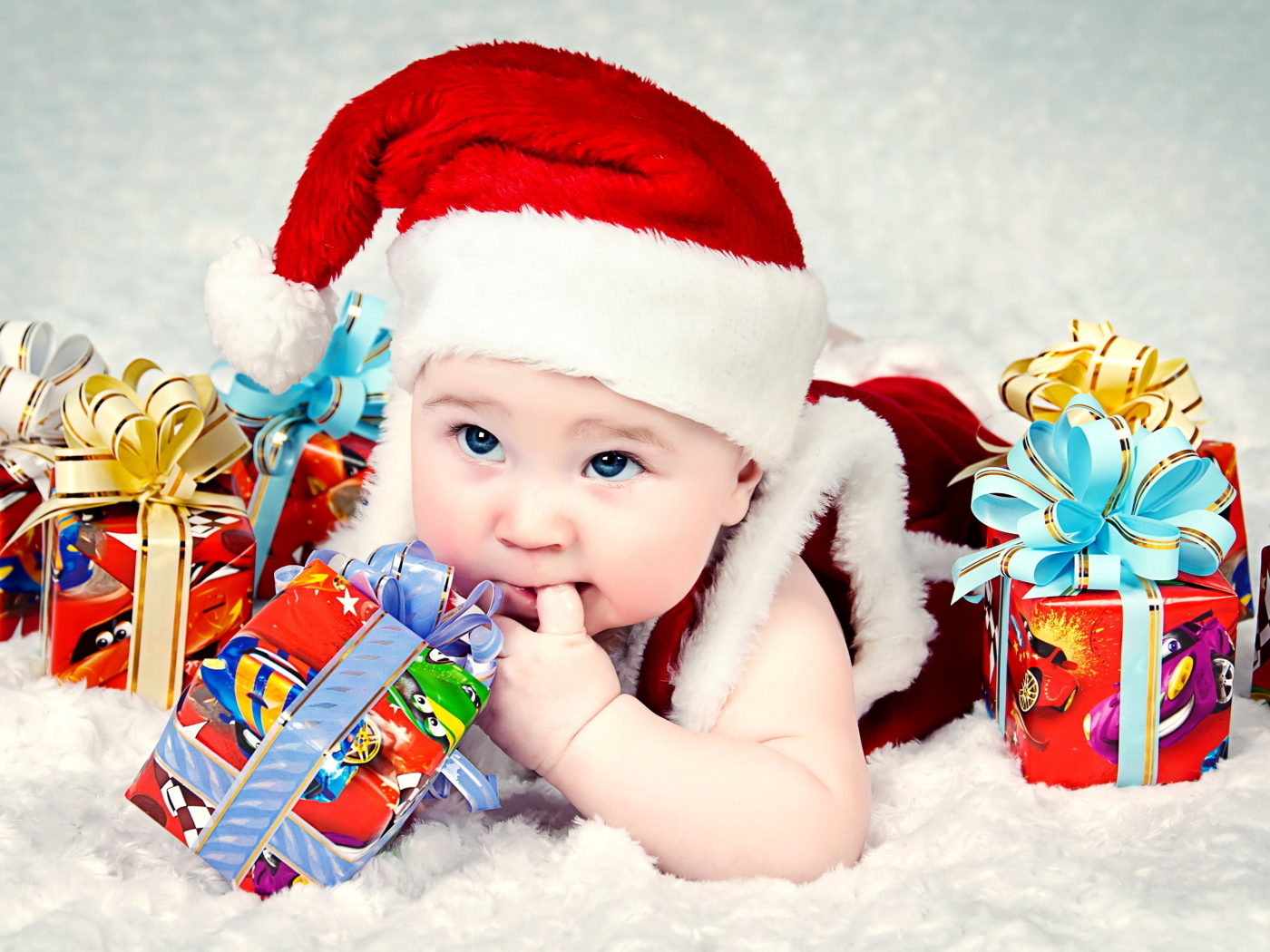 Грудной ребенок в новогодней шапке с подарками на покрывале
