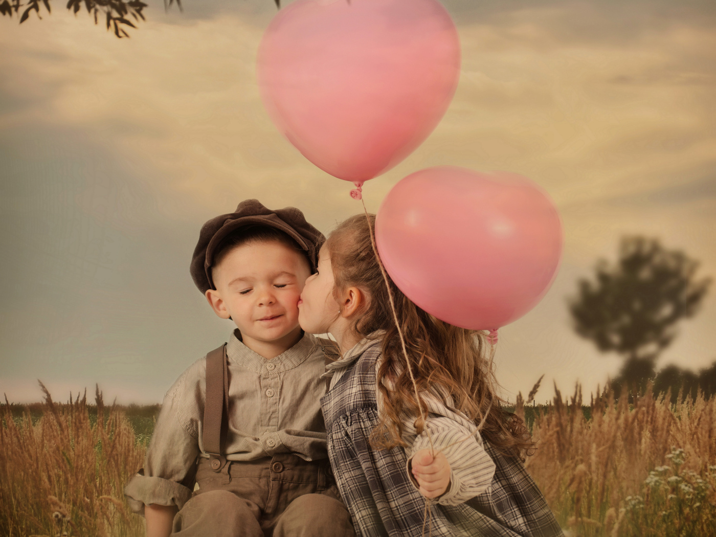 Маленькая девочка с шариками целует мальчика