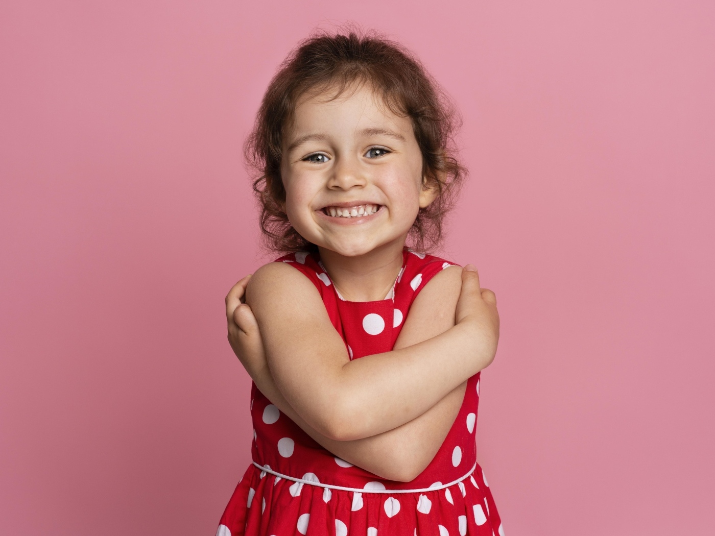 Улыбающаяся маленькая девочка в красном платье на розовом фоне